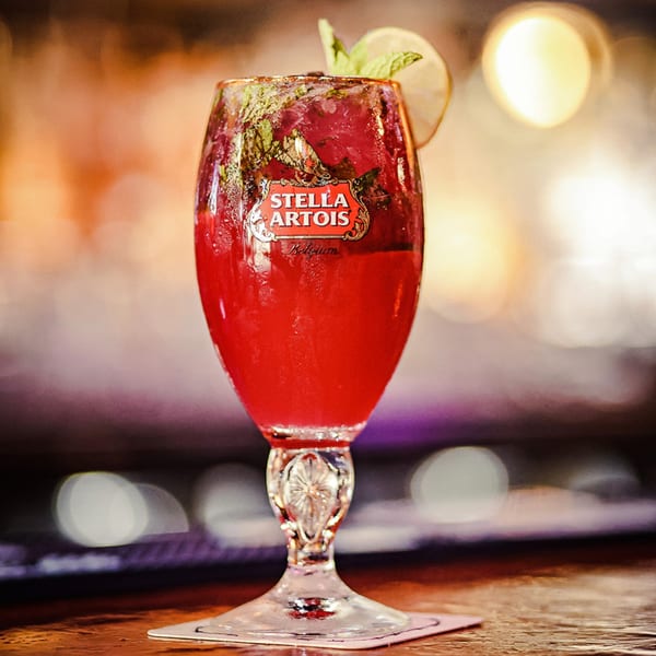 A Stella Artois glass filled with a red cocktail, garnished with mint and lime, on a bar.