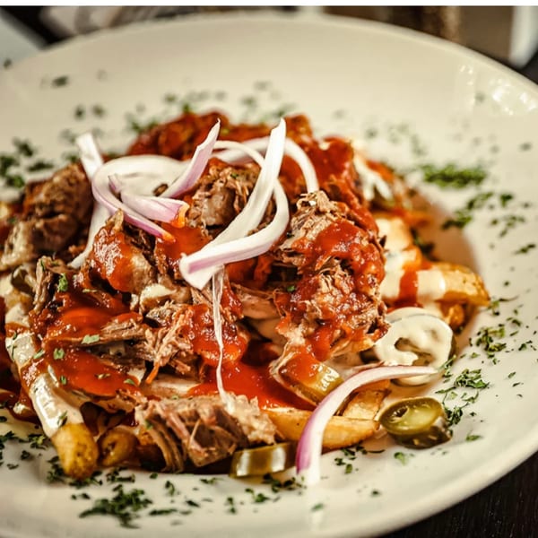 Pulled pork nachos with red sauce, white sauce, red onions, and jalapeños on a white plate.