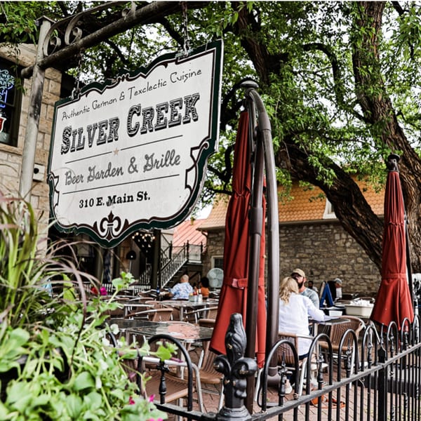 Silver Creek Beer Garden & Grille sign above an outdoor patio with diners and red umbrellas.