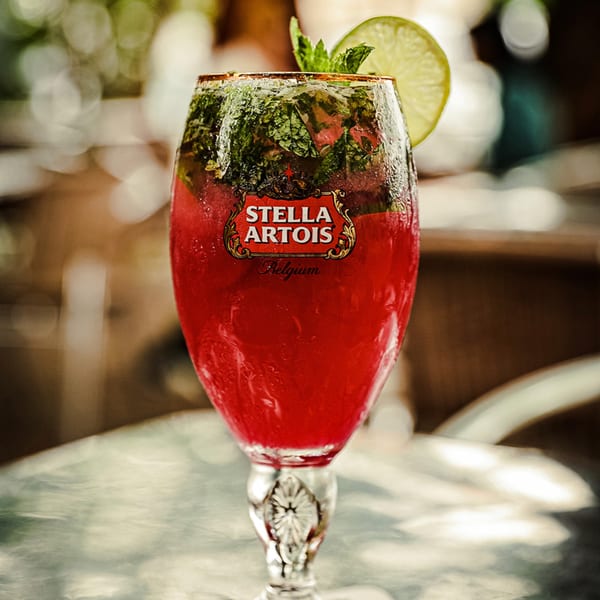 A Stella Artois glass filled with a red cocktail, garnished with mint and a lime slice.