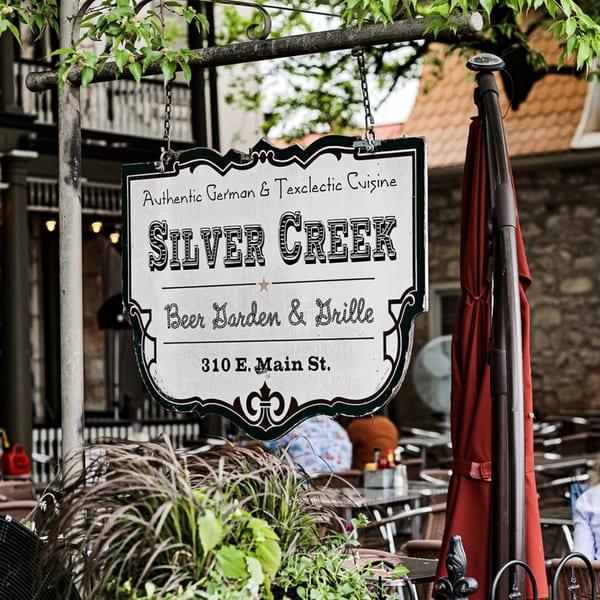 Silver Creek Beer Garden & Grille sign hanging above an outdoor patio with tables and red umbrella.