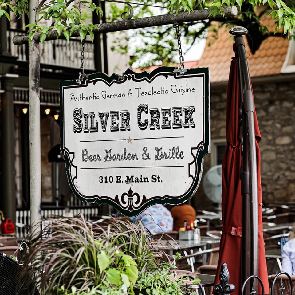 Silver Creek Beer Garden & Grille sign hanging above an outdoor patio with tables and red umbrella.