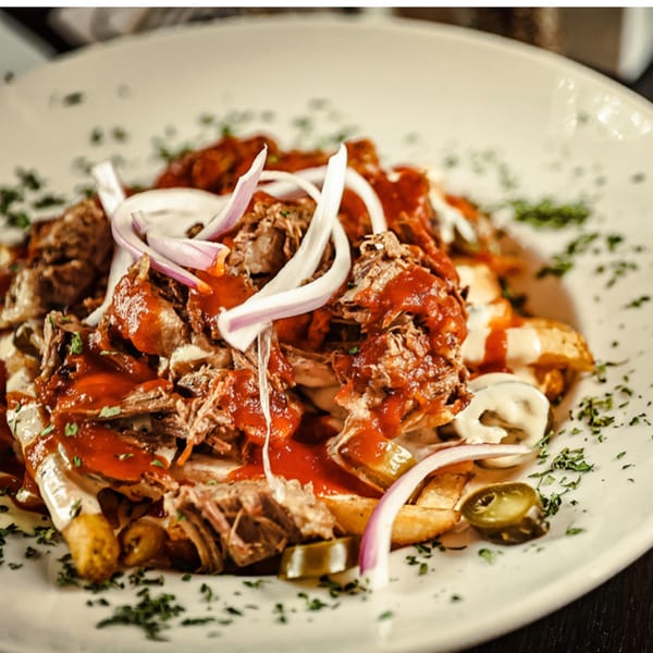 Loaded fries topped with shredded meat, red sauce, white sauce, red onions, and jalapeños.