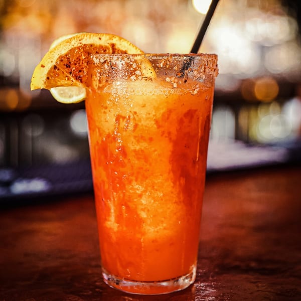 A vibrant orange cocktail with a salted rim, garnished with a lime and orange slice, on a bar.