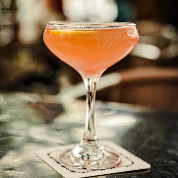 A vibrant orange cocktail in a stemmed glass with a lemon slice, on a coaster at Silver Creek Beer Garden & Grille.